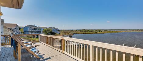 A wooden deck with a railing overlooking a body of water, with houses in the background.