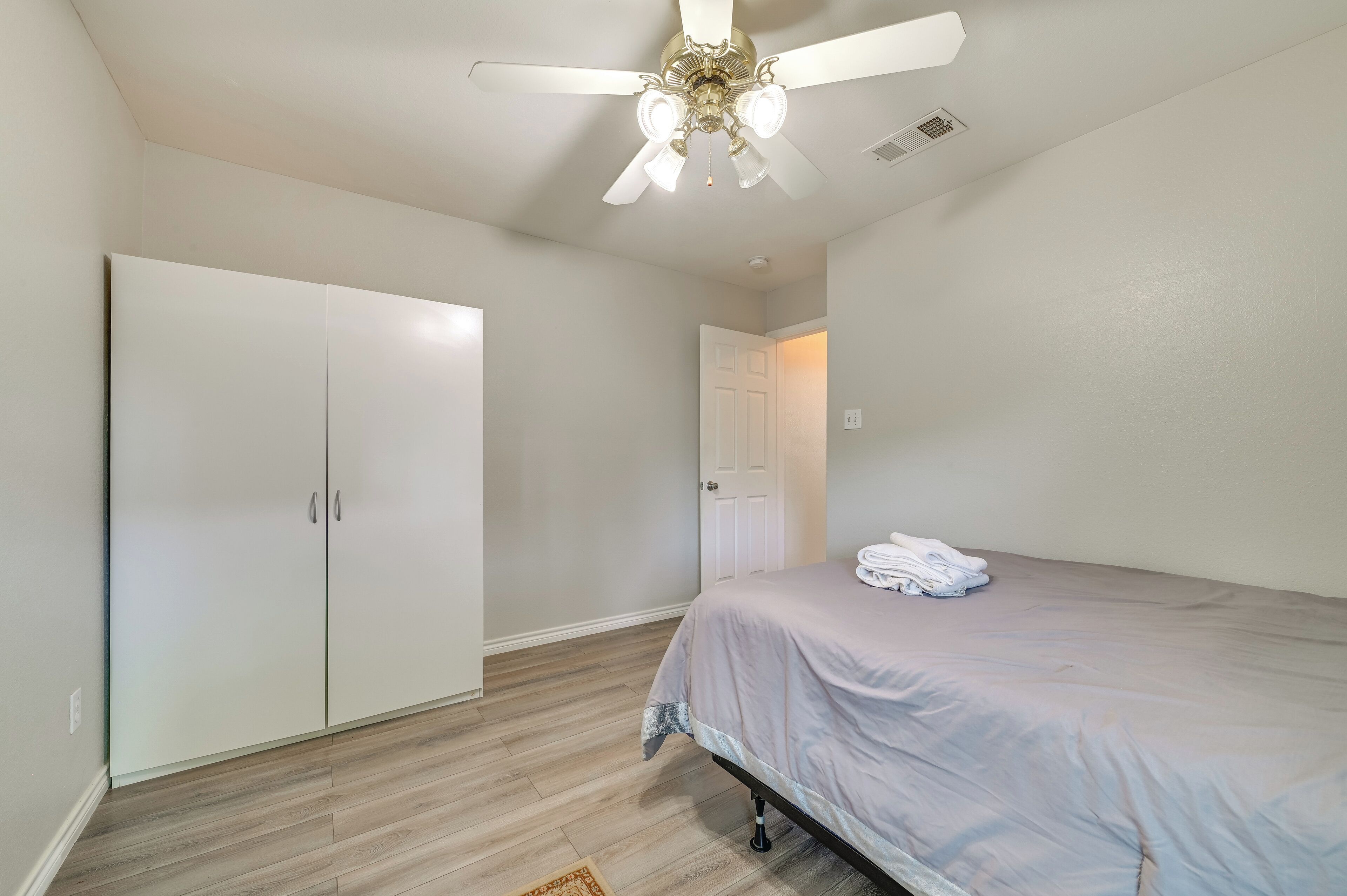 A bedroom with a bed, a ceiling fan, a wardrobe, and a door leading to another room.