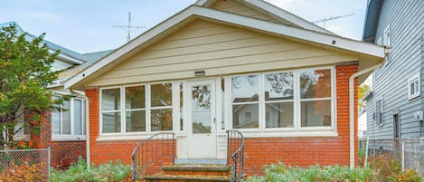 A single-story house with a front porch, a brick exterior, and a white door.