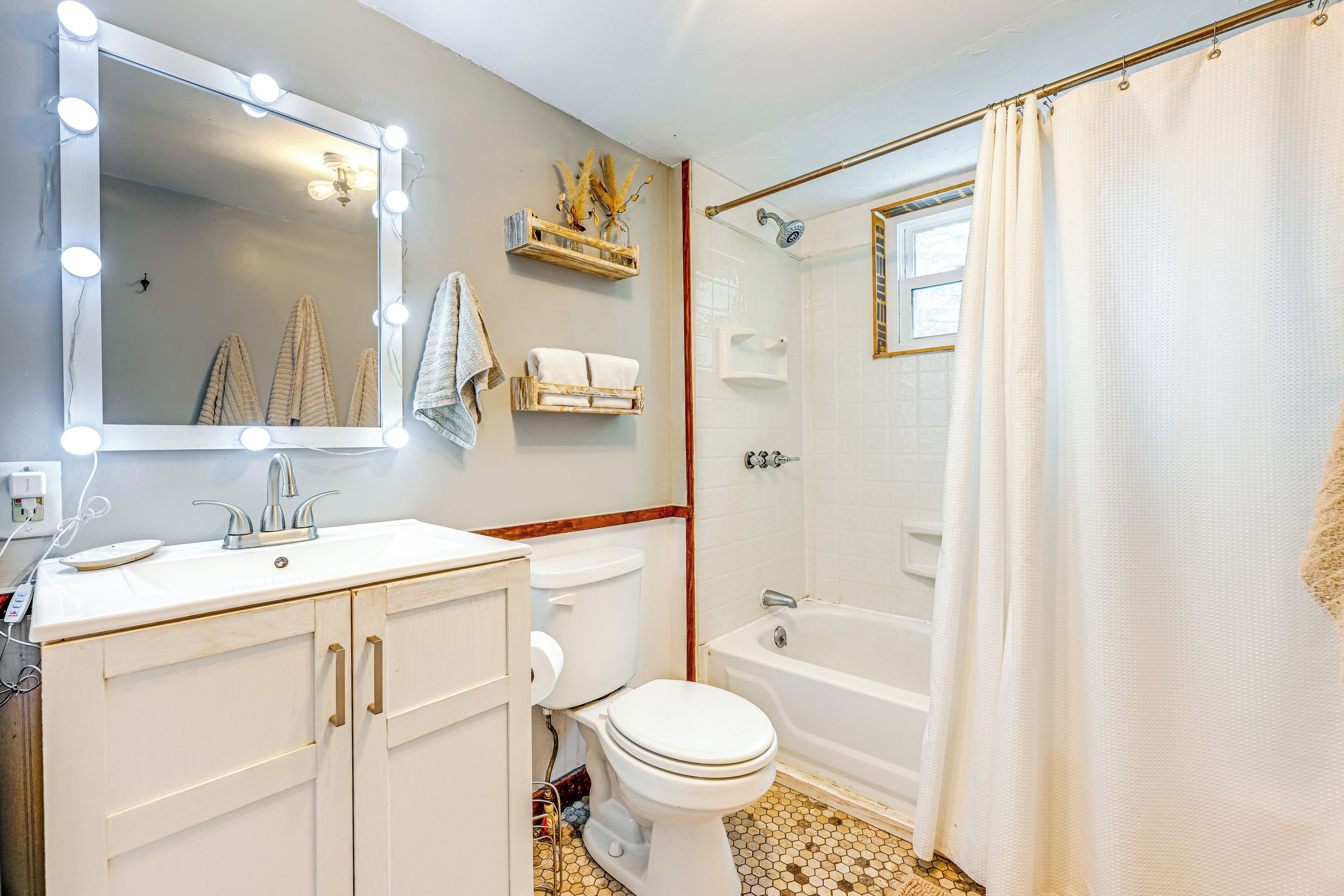 A bathroom with a vanity, mirror, lights, toilet, and bathtub.