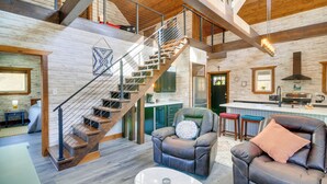 A spacious living area with a wooden staircase, leather recliner, and a kitchen in the background. - Hike & Climb: Pet-friendly Red River Gorge Cabin! (Beattyville)