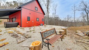 A red barn with a black roof, a wooden bench, and a gravel path with scattered stones. - Hike & Climb: Pet-friendly Red River Gorge Cabin! (Beattyville)