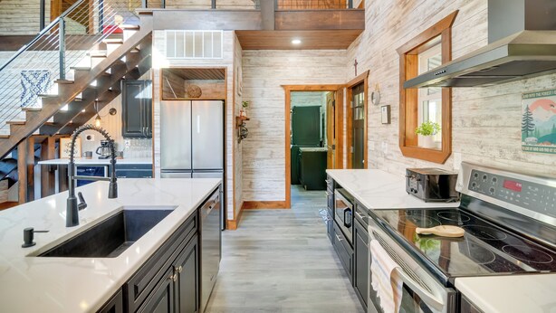 A modern kitchen with a central island, stainless steel appliances, and a wooden staircase. - Hike & Climb: Pet-friendly Red River Gorge Cabin! (Beattyville)