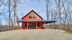 A red building with a covered porch and large windows, surrounded by trees. - Hike & Climb: Pet-friendly Red River Gorge Cabin! (Beattyville)
