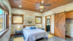A bedroom with a large bed, wooden walls, a ceiling fan, and a sliding barn-style door. - Hike & Climb: Pet-friendly Red River Gorge Cabin! (Beattyville)