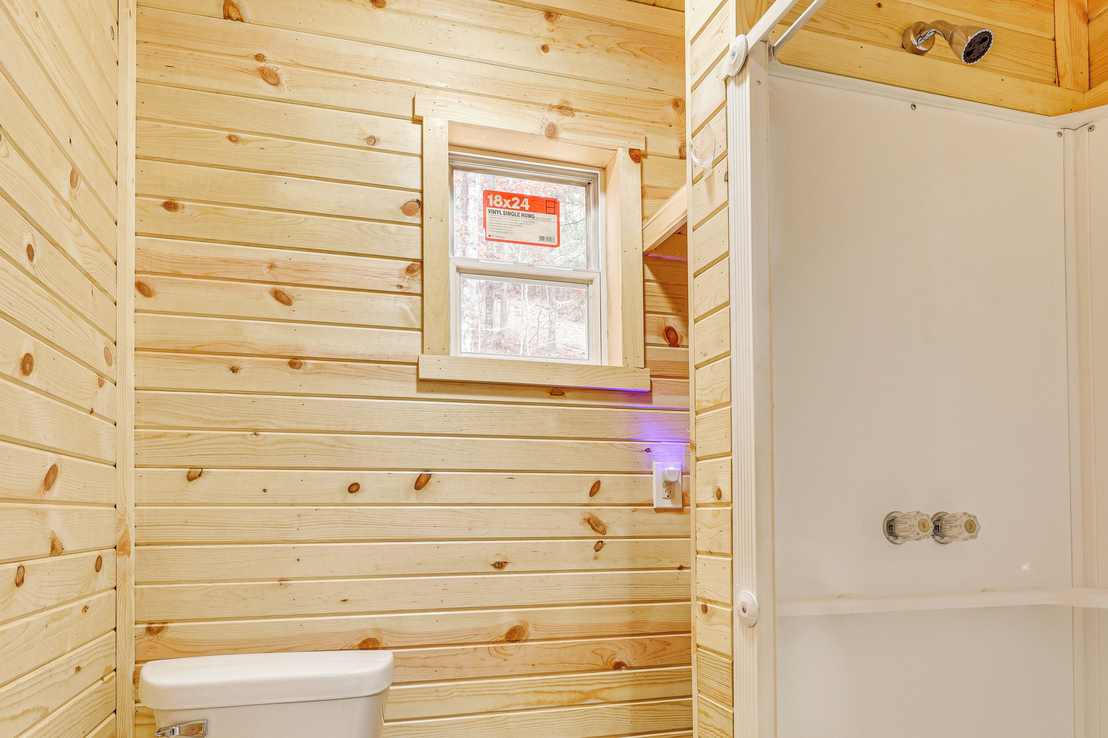A wooden-paneled bathroom with a toilet, a window, and a shower door.