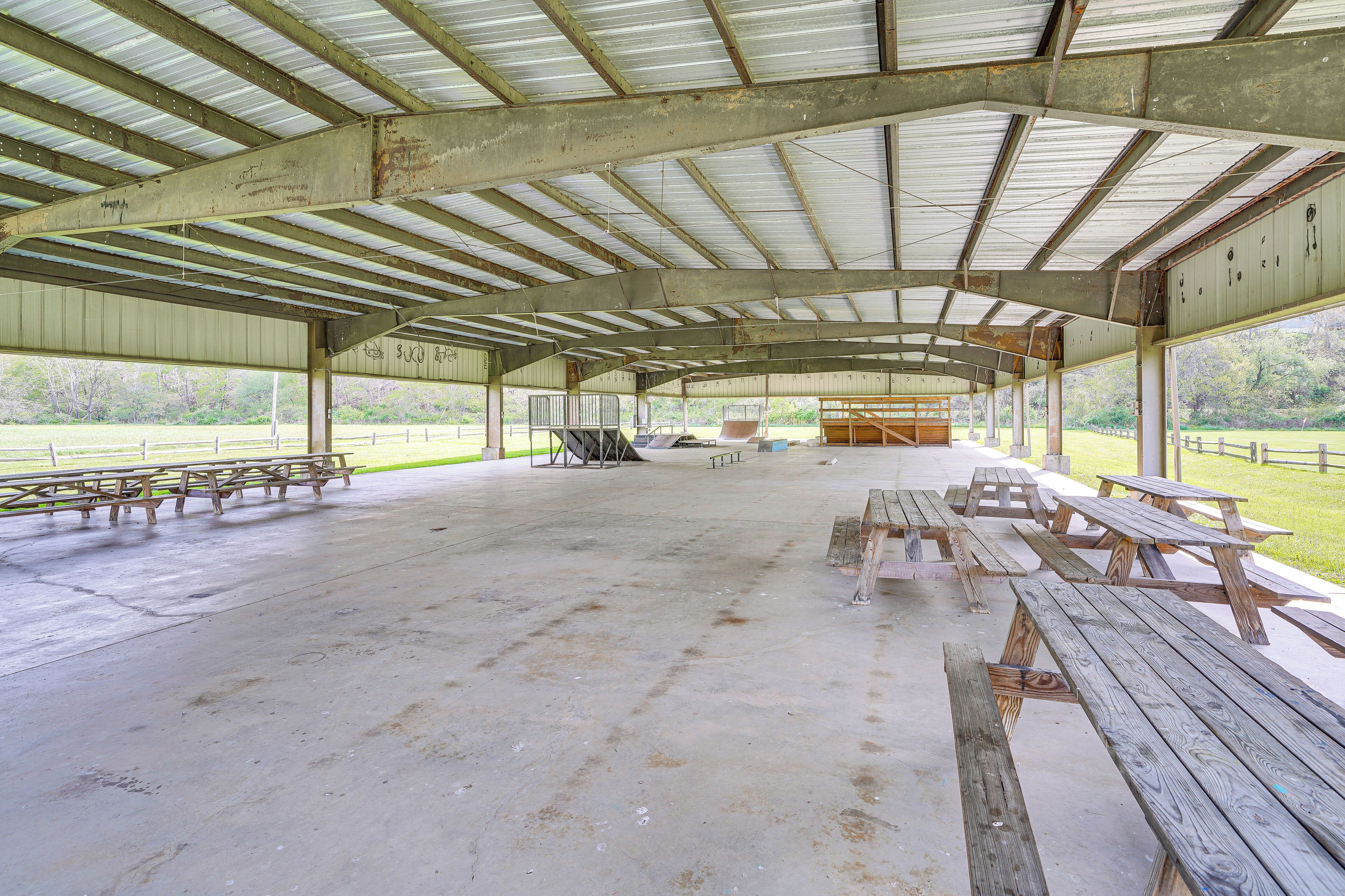 A covered picnic area with wooden benches and picnic tables, featuring a concrete floor and metal roof structure.