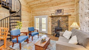 A wooden cabin interior with a staircase, a stone fireplace, a sofa, and a coffee table. - Near Greenbrier River! Mtn-view Cabin w/ Fire Pit (Marlinton)