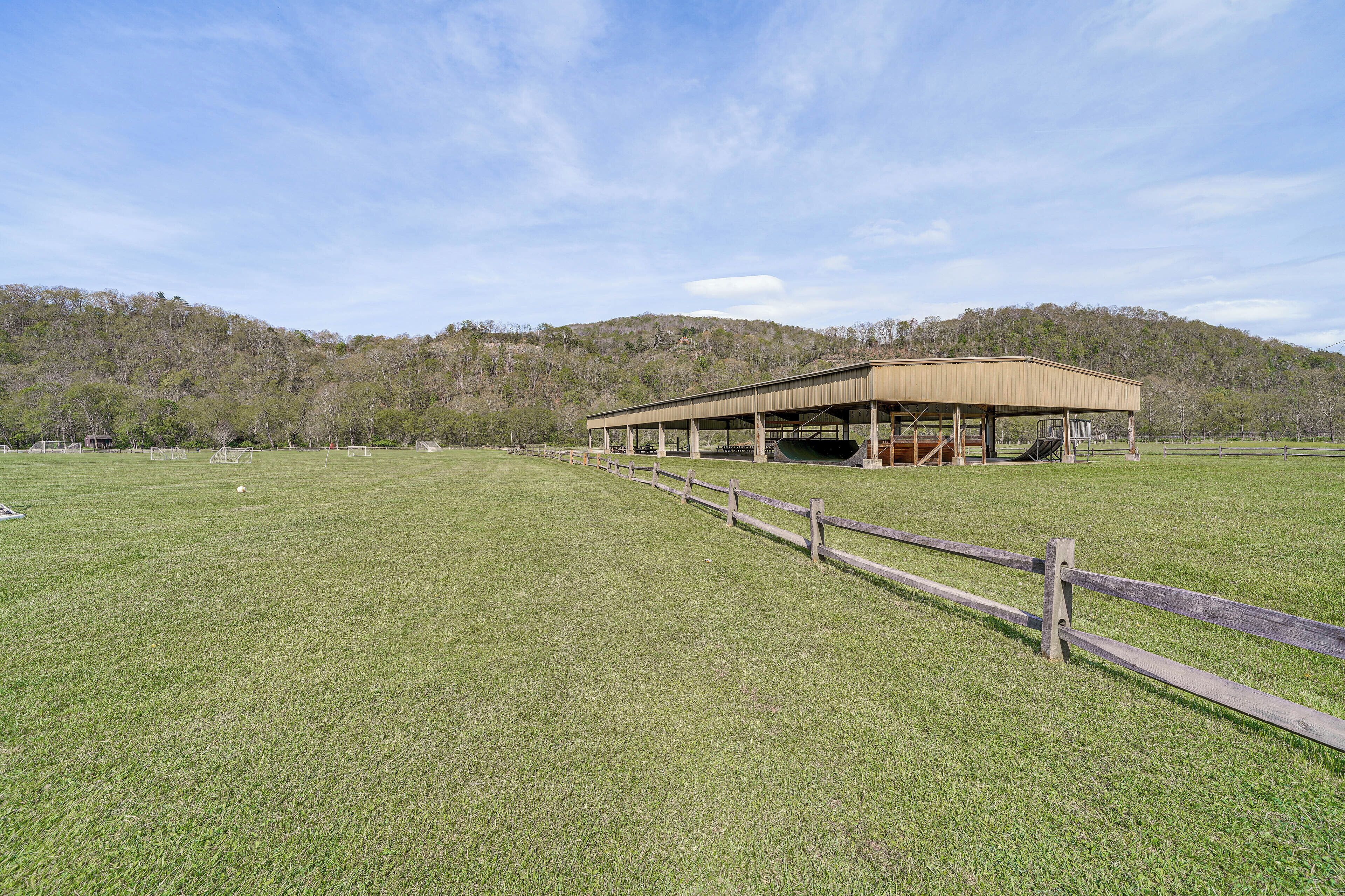 A large, open grassy field with a wooden fence leading to a covered structure.