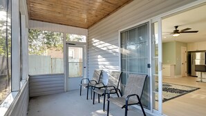 A covered porch with four chairs, a sliding glass door leading to a kitchen, and a ceiling fan. - 1 Mi to Pier: Screened Patio at Murrells Inlet Apt (Murrells Inlet)