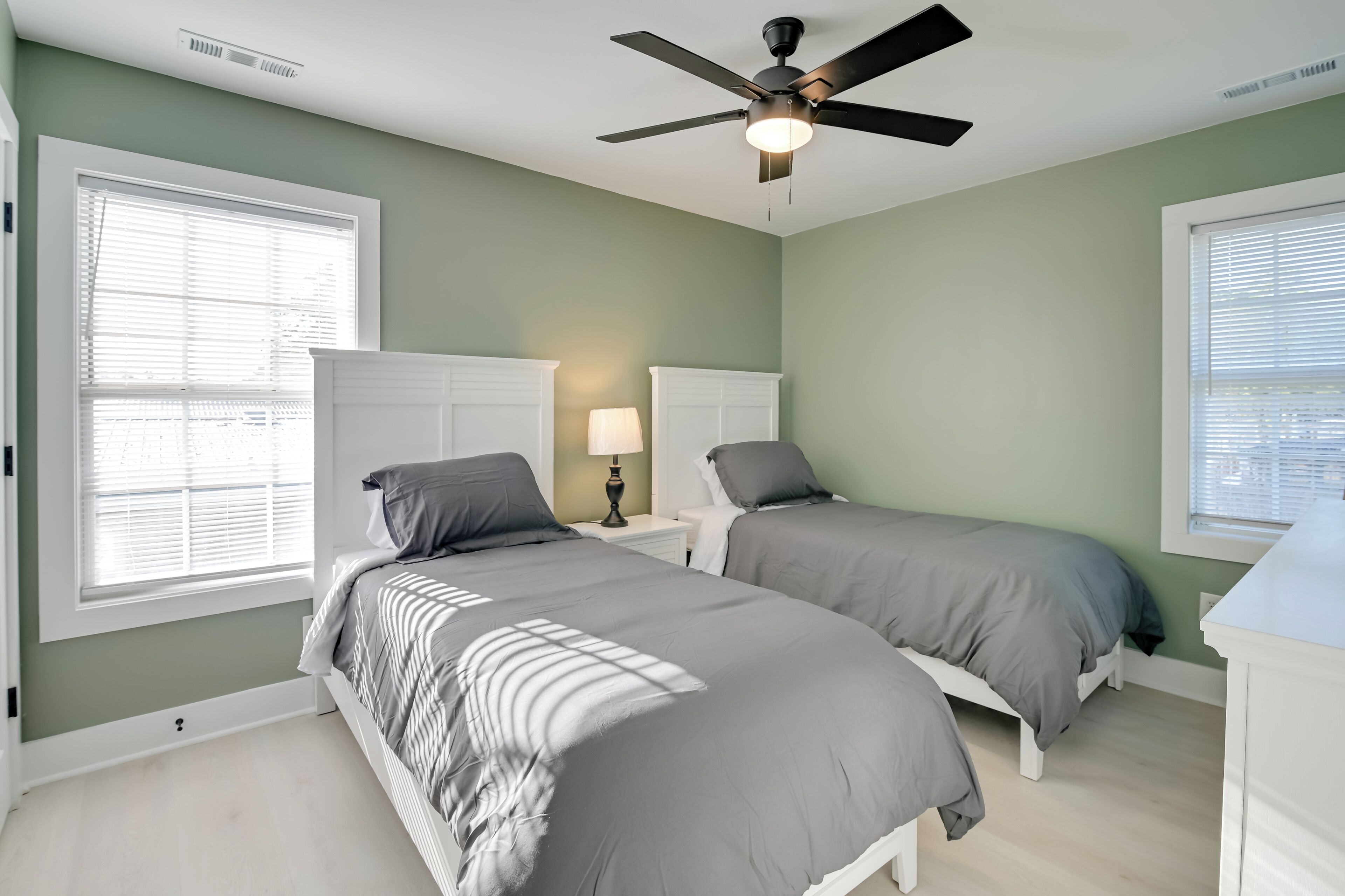 A bedroom with two beds, a ceiling fan, and a window with blinds.