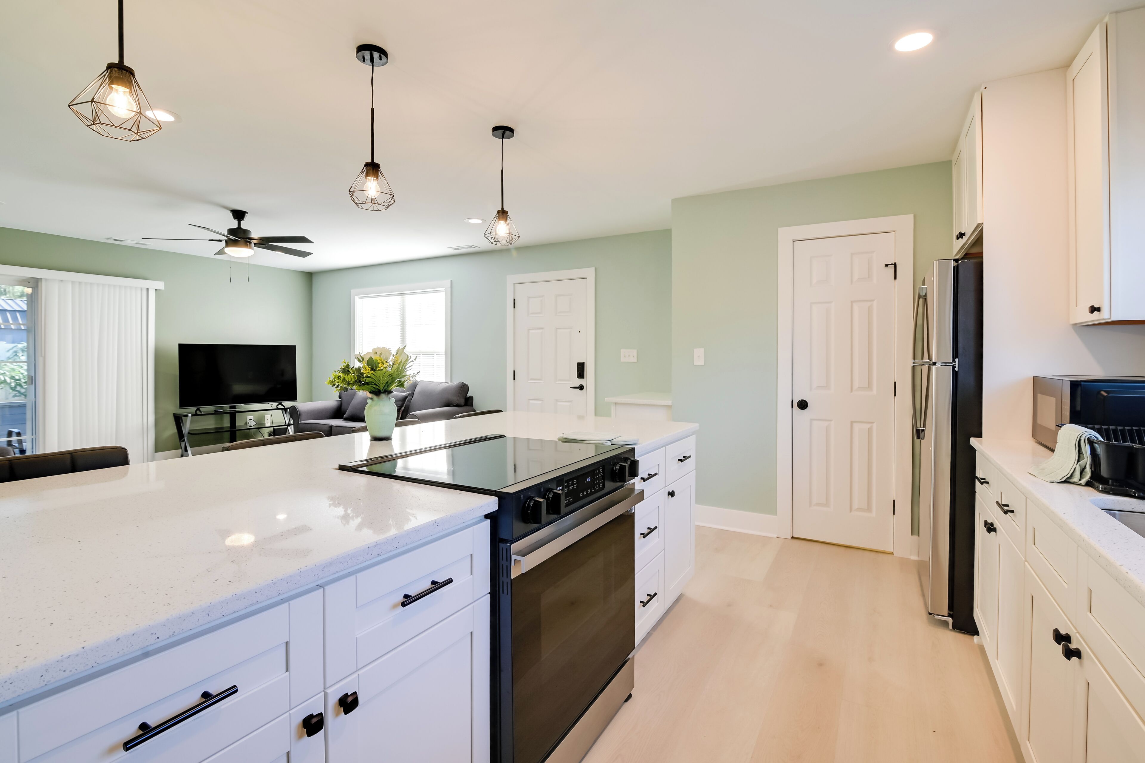 A modern kitchen with white cabinetry, a black stove, and a built-in oven. There are pendant lights, a ceiling fan, and a large window.