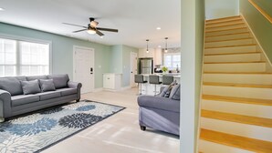 A spacious living area with a grey sofa, a patterned rug, a ceiling fan, and a kitchen in the background. - 1 Mi to Pier: Screened Patio at Murrells Inlet Apt (Murrells Inlet)