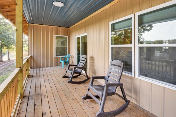 Une terrasse en bois, agrémentée de fauteuils à bascule et d’une table, et protégée par un toit en métal et des murs en bois.