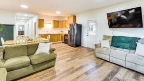 A spacious living area with a sofa, a dining table with chairs, a kitchen with wooden cabinets, a refrigerator, and a TV mounted on the wall. - Lake-view Home in Statham w/ On-site Fishing (Statham)