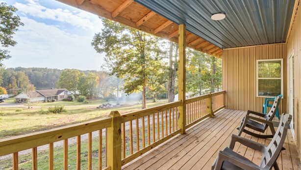 A covered porch with wooden railings, a view of a residential area, and a few outdoor chairs. - Lake-view Home in Statham w/ On-site Fishing (Statham)