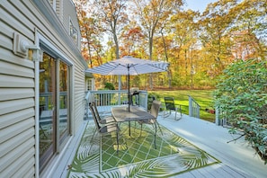 Relax on the covered deck surrounded by a lush garden with a metal table and chairs under a striped umbrella.