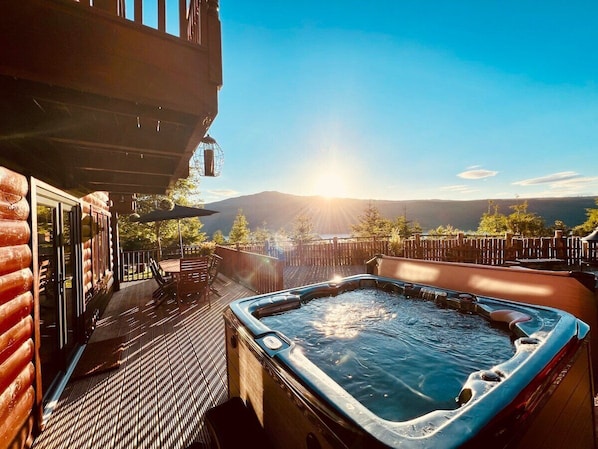 A hot tub on a wooden deck with a view of mountains and a clear sky. - Lodges On Loch Ness (Inverness)