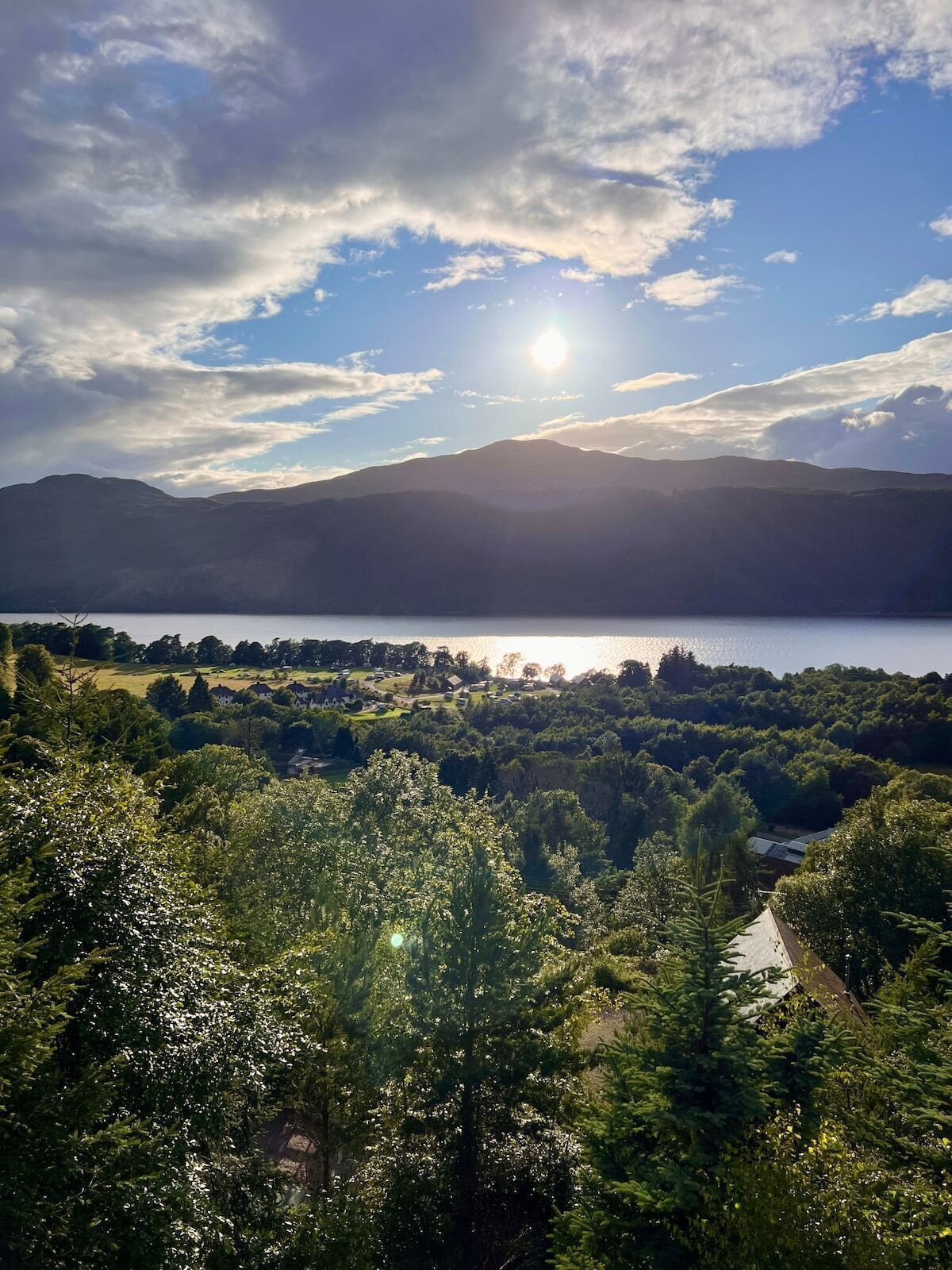 En sjö med berg i bakgrunden, omgiven av tät vegetation och några få byggnader.