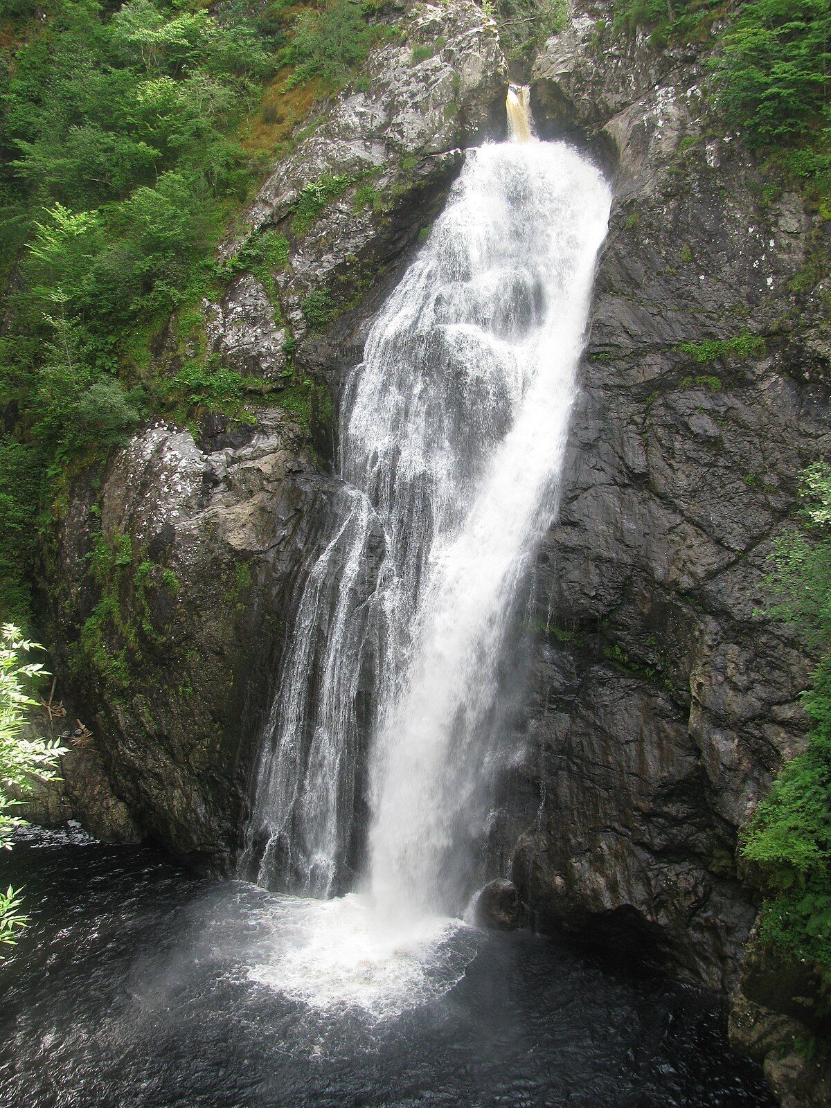 Uma cascata descendo por um penhasco rochoso, rodeada por vegetação exuberante.