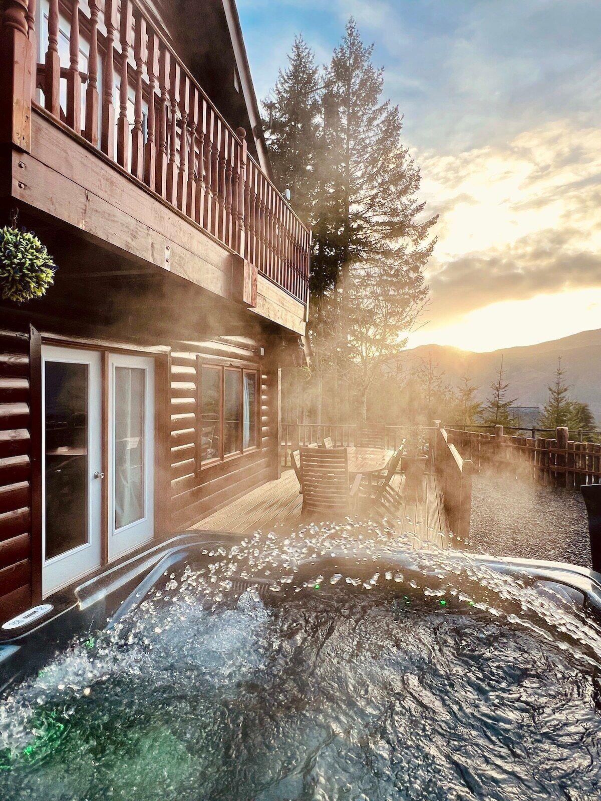 Una cabaña de madera con balcón, jacuzzi y vistas a árboles y montañas.