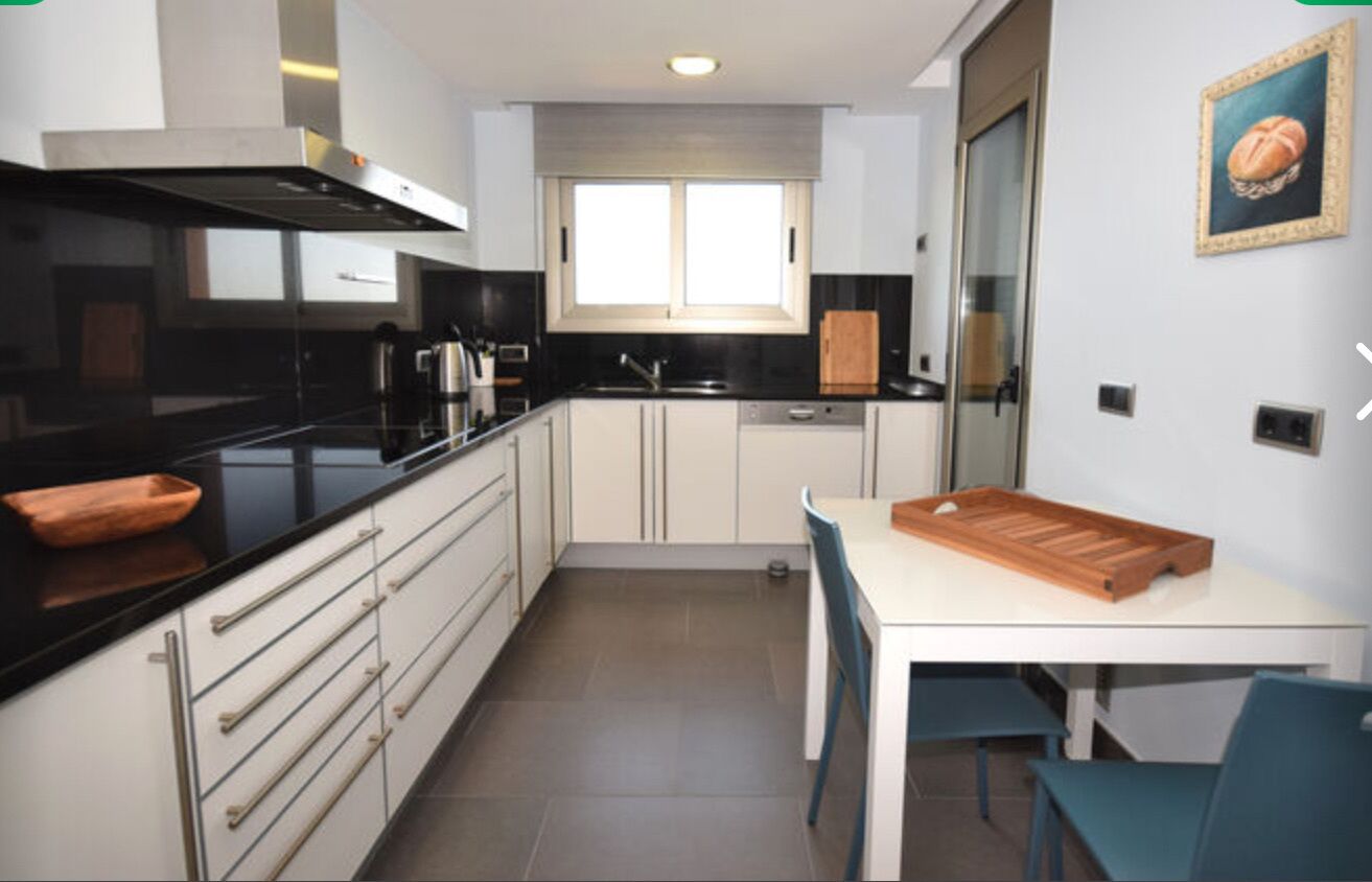 A modern kitchen with white cabinets, black countertops, and a wooden dining table.