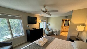A hotel room with a bed, a desk, a chair, a television, and a ceiling fan.