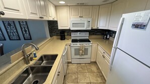 A compact kitchen with white cabinets, a stainless steel sink, a microwave, an oven, and a refrigerator.