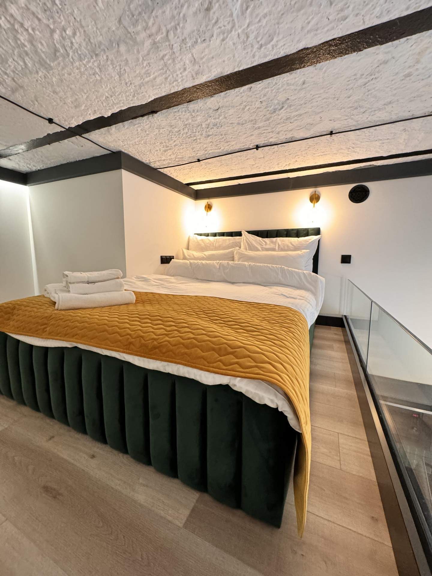 Une chambre moderne avec un grand lit, un plancher en bois et un plafond blanc à texture.