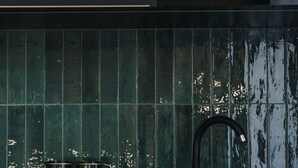 A kitchen with a black stove, a sink, and a backsplash with green tiles.