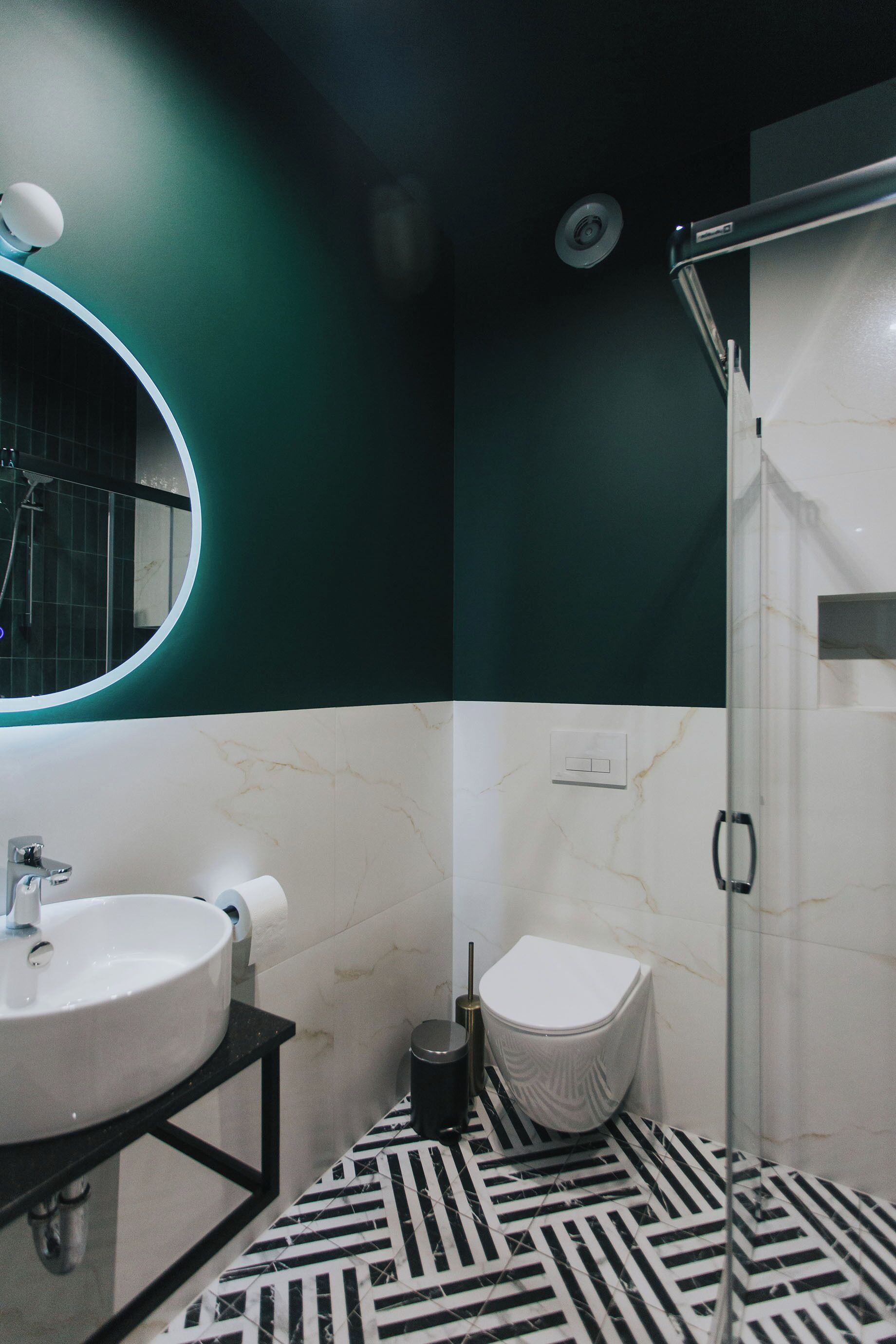 Un bagno moderno con uno specchio rotondo, un lavandino, un WC e una zona doccia.