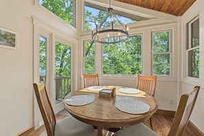 A sunroom with a wooden table, chairs, and a chandelier.