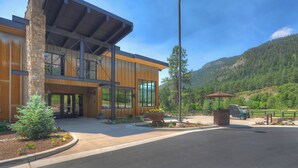 A modern building with large windows and a stone facade, surrounded by a landscaped area with a mountain backdrop. - High Mountain Home | AC, Pool, Hot Tub, Golf & Ski (Durango)