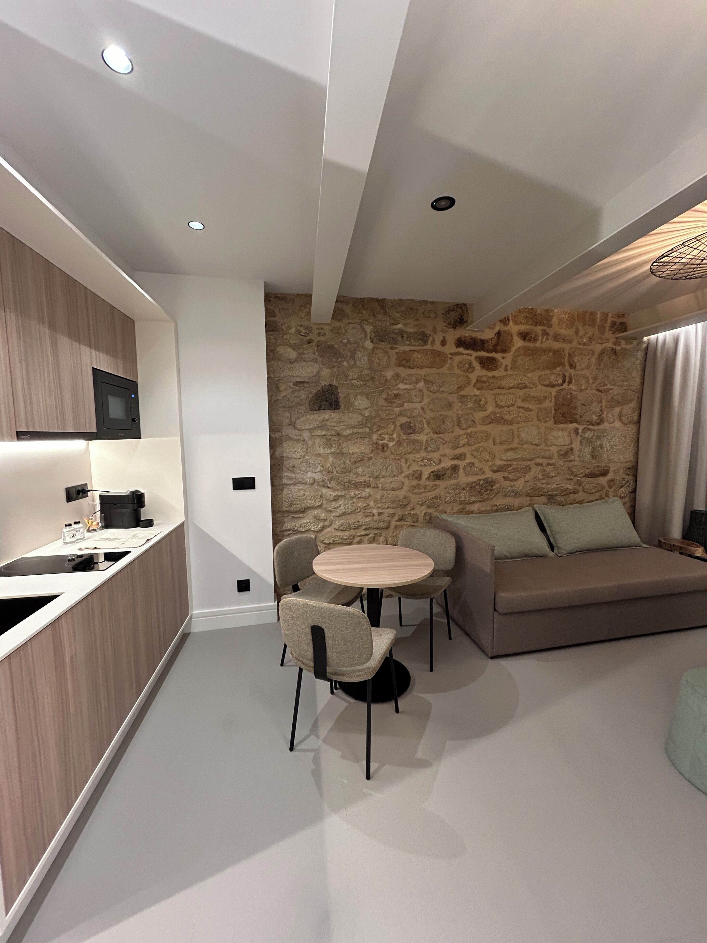 Een moderne keuken met inbouwapparatuur, een accentmuur van steen, een ronde eettafel met stoelen en een bank met kussens.