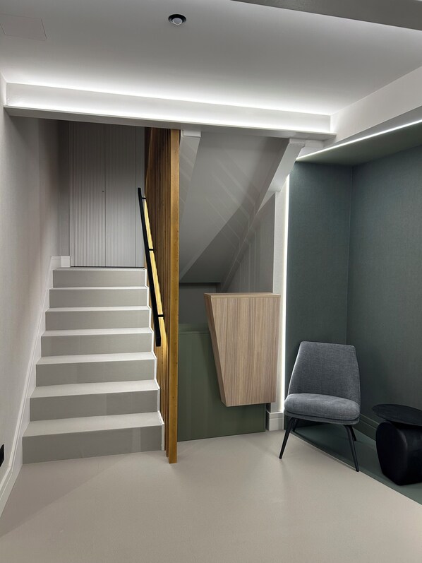 A modern interior with a staircase, a wooden panel wall, a grey chair, and a small black table. - INTRAMUROS Quiet Apartments (Muros)