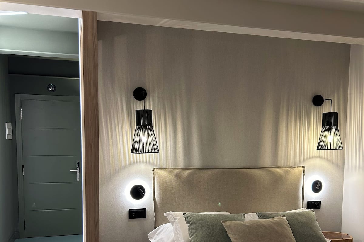 A modern bedroom with a large bed, two bedside lamps, a round table, and a door leading to another room.