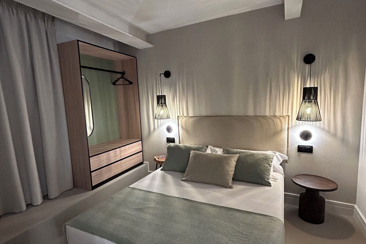 A modern hotel room with a large bed, a bedside table, a round table, a mirror, and two wall-mounted lamps.