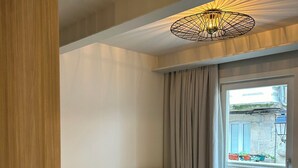 A modern room with a sofa, two ottomans, a hanging light fixture, and a window with a view of buildings. - INTRAMUROS Quiet Apartments (Muros)