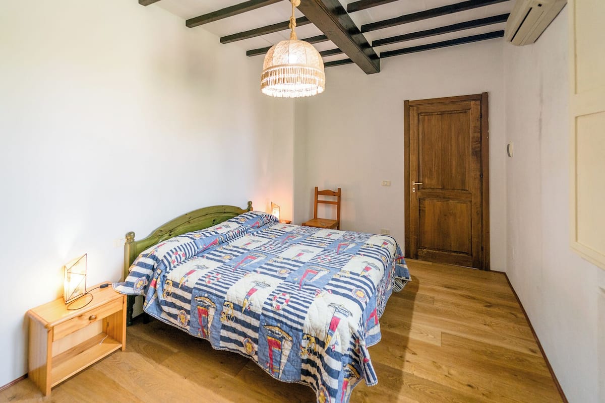 Een slaapkamer met een houten bed, een nachtkastje met een lamp, een houten stoel en een houten deur.