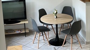 A modern living room with a round wooden table, four black chairs, a flat-screen TV, a woven pendant light, and a framed leaf artwork on the wall. - Beautiful T3 bis duplex near town center (Sens)