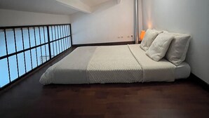 A minimalist bedroom with a large bed, a nightstand, a lamp, and a view through a window with a grid pattern. - Beautiful T3 bis duplex near town center (Sens)
