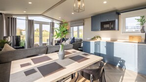 A modern kitchen with blue cabinets, a dining area with a wooden table and chairs, and a large window with curtains. - Host Stay Riverwood Ashdown Retreat (Pickering)