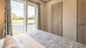 A bedroom with a large bed, a window with curtains, a wardrobe, and a view of the outdoors. - Host Stay Riverwood Ashdown Retreat (Pickering)