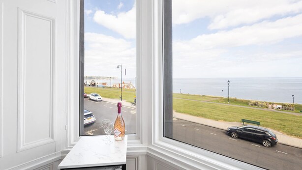 A view from a window with a white interior, overlooking a road with cars and a grassy area with a bench. - Host Stay Egton Bridge at the Sandbeck (Whitby)