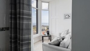 A modern room with a grey sofa, a small table with a kettle, and a view of the sea through large windows. - Host Stay Egton Bridge at the Sandbeck (Whitby)