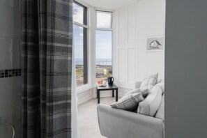A modern room with a grey sofa, a small table with a kettle, and a view of the sea through large windows. - Host Stay Egton Bridge at the Sandbeck (Whitby)