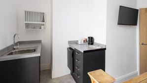 A compact kitchen with a built-in sink, a small countertop, a microwave, and a coffee maker. There is a wooden stool and a television mounted on the wall. - Host Stay Grosmont at the Sandbeck (Whitby)