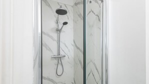 A glass-enclosed shower with a handheld showerhead and a fixed showerhead, set against a marble wall. - Host Stay Grosmont at the Sandbeck (Whitby)