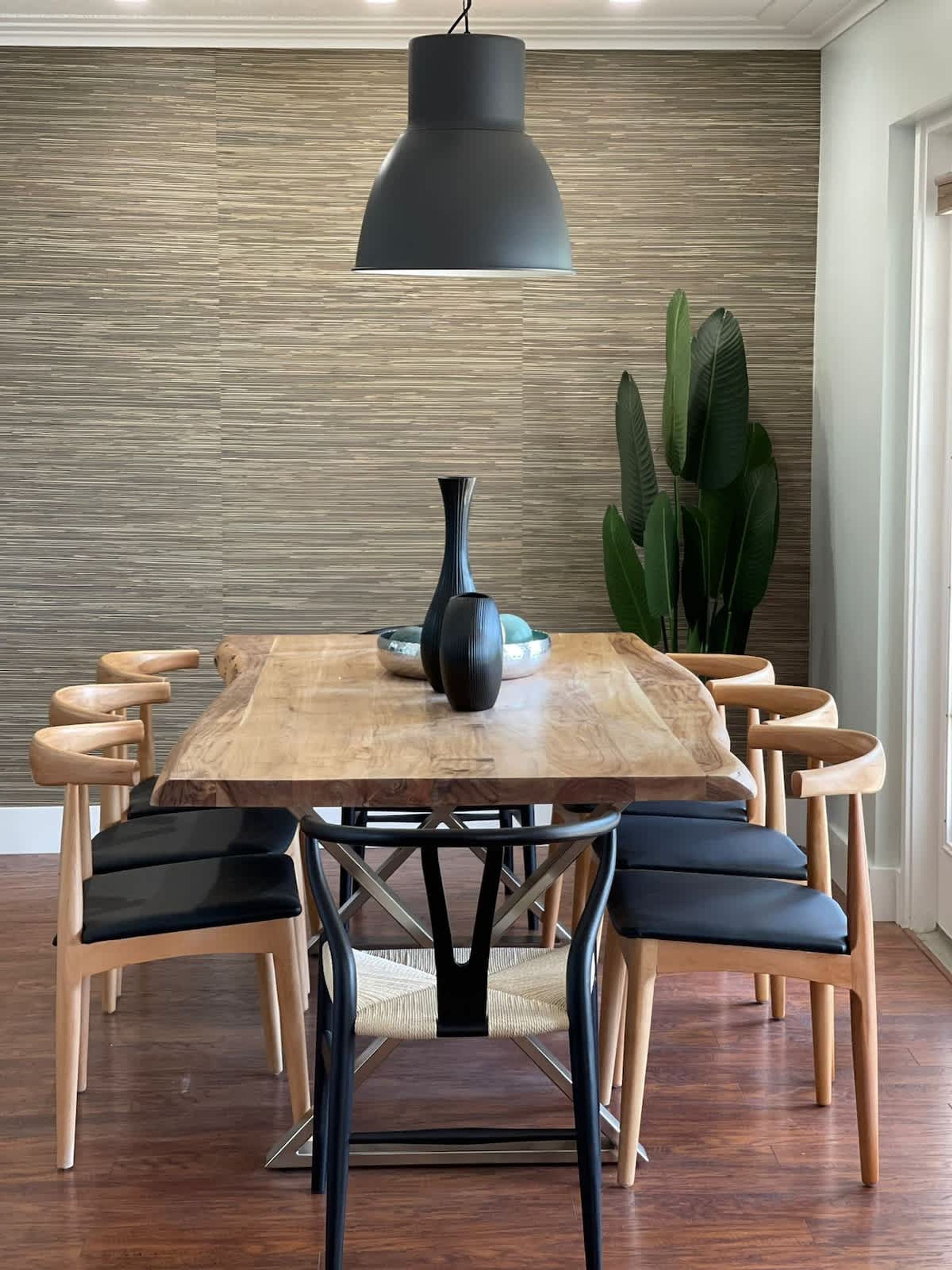 A dining table with a black pendant light, surrounded by wooden chairs with black cushions.