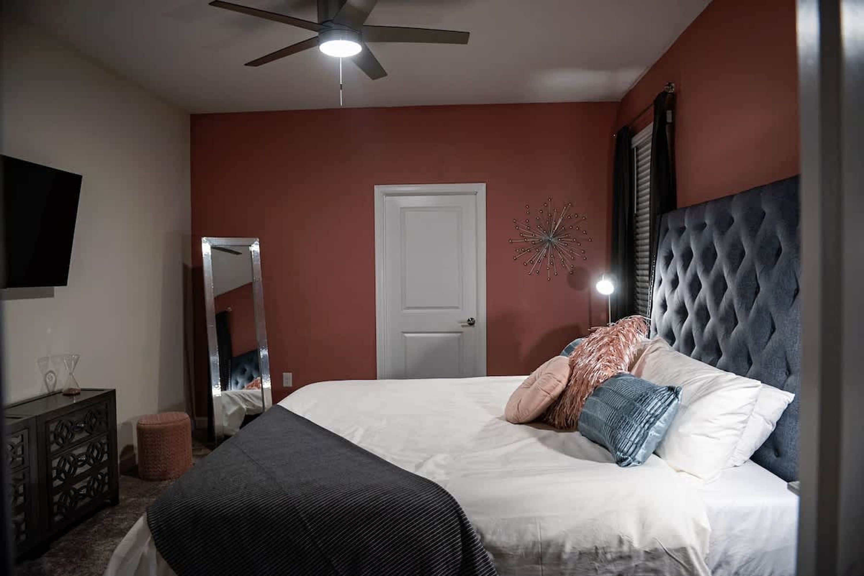 Ein Schlafzimmer mit Bett, Deckenventilator, Spiegel, Tür und Wandfernseher.